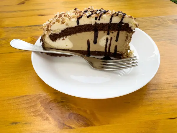 Çikolatalı kek dilimi beyaz tabakta çiselemeli ahşap masada..