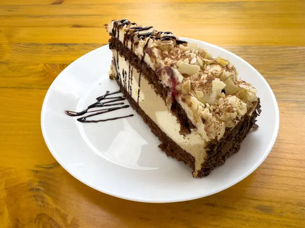 Çikolatalı fındıklı kek dilimi, beyaz tabakta serpiştirilmiş tahta masa.