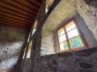 Ahşap tavanlı taştan bir iç döşeme ve güneşli ahşap pencereli..