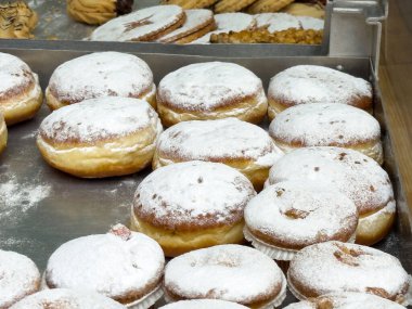 Pişirme tepsisinde pudra şekerli çörekler ve arka planda çeşitli kurabiyeler..