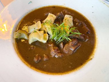 Şehriyeli biftek güveci ve beyaz kasede taze otlar..