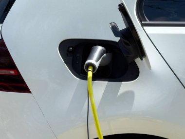Beyaz araçta sarı kabloyla elektrik yükleme portu.
