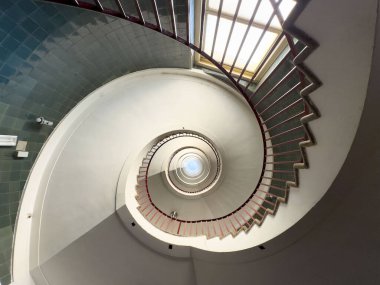 Kırmızı parmaklıklı sarmal merdiven ve yukarıdan gelen doğal ışık..