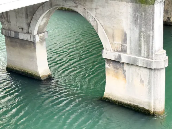 Sakin yeşil nehir suyunun üzerindeki taş köprü kemeri.