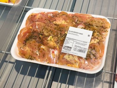 Tarvisio, İtalya - 01 Haziran 2025: Plastik tepside salamura edilmiş tavuk filetoları, mutfak ilhamı için bakkaldaki metal raflarda sergileniyor