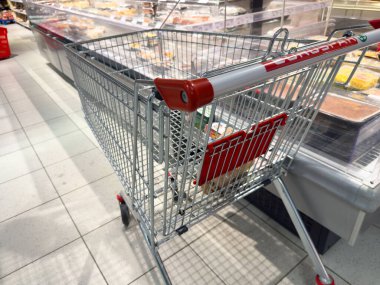 Tarvisio, İtalya - 01 Haziran 2025: Süpermarket koridorunda yer alan alışveriş arabası, gıda ürünleri ve canlı vitrinlerle çevrili, perakende atmosferi vurguluyor