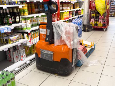 Tarvisio, İtalya - 01 Haziran 2025: Elektrikli palet krikosu marketteki içecek rafları, lojistik ve envanter arasında yer alan plastiğe sarılı