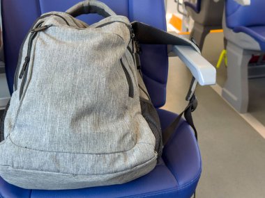 Venedik, İtalya - 25 Haziran 2025: Gri sırt çantası tren vagonunda mavi koltuğa yerleştirilmiş, seyahat gereksinimlerini temsil ediyor ve şehir içi seyahatleri taklit alanı ile temsil ediyor.