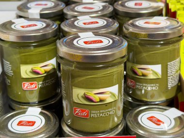 Venedik, İtalya - 23 Haziran 2025: Pasti şam fıstığı serpiştirilmiş kavanozlar bir süpermarket rafında sergileniyor, çekici ambalajları ve zengin yeşil renkleri vurgulanıyor