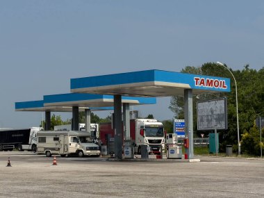 Venedik, İtalya - 23 Haziran 2025: Tamoil yakıt istasyonu, açık mavi gökyüzü ve yemyeşil alana karşı park edilmiş birden fazla pompa ve araç barındırıyor