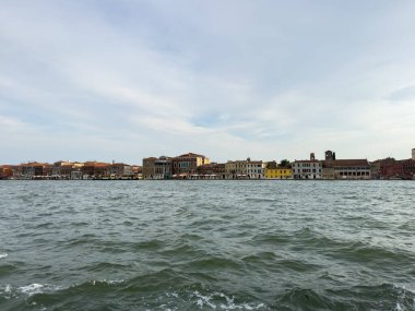 Venedik, İtalya - 23 Haziran 2025: Venedik 'in renkli binalarla çevrili sahili manzarası, sakin ve resimsel bir ortam yaratıyor.