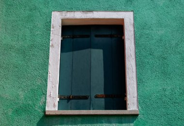 Yeşil sıva duvarında kapalı ahşap kepenkli pencere.