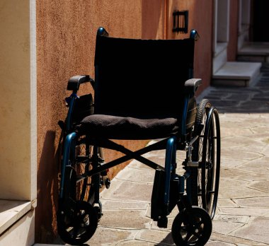 Burano, İtalya - 25 Haziran 2025: Güneşli bir günde bir duvara yaslanmış tekerlekli sandalye, kentsel ortamlarda ulaşılabilirlik ve bağımsızlık temaları vurgulanıyor