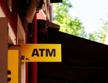 Burano, İtalya - 25 Haziran 2025: Ağaçlar ve kentsel unsurlarla çevrili binada gösterilen sarı ATM işareti, nakit çekilmesi için ulaşılabilirliği vurguluyor