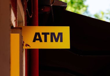 Burano, İtalya - 25 Haziran 2025: Yeşillik ile çevrili bir duvarda göze çarpan sarı ATM işareti, nakit çekilme noktasını gösteriyor