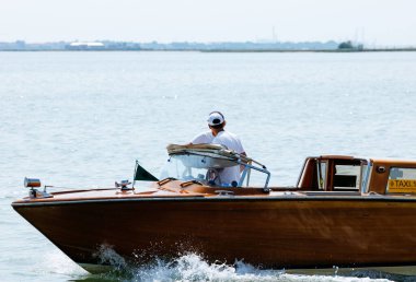 Burano, İtalya - 25 Haziran 2025: İnsanoğlu sakin sularda, güneşli bir günde huzurlu bir atmosferin tadını çıkararak ahşap bir teknede geziniyor.