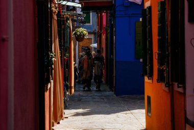 Burano, İtalya - 25 Haziran 2025: Burano, İtalya 'da dar bir sokak, bu eşsiz adanın canlı atmosferinin keyfini çıkaran renkli binalar ve turistlere ev sahipliği yapıyor.