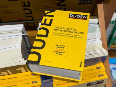 Villach, Avusturya - 01 Temmuz 2025: Duden sözlüğü, açık sarı kapaklı ve çevresindeki kitaplarla birlikte, dil öğrenmeyi vurgulayarak kitapçıda belirgin bir şekilde sergilendi