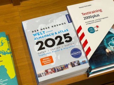 Villach, Avusturya - 01 Temmuz 2025: Kosmos tarafından Almanac ve Atlas 2025 küresel bilgi ve gerçekleri vurgulayan çeşitli kitaplarla birlikte ahşap bir rafa yerleştirildi
