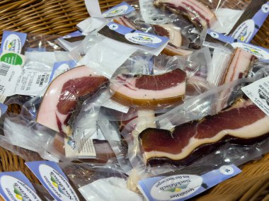 Villach, Avusturya - 01 Temmuz 2025: Çeşitli gurme domuz pastırması paketleri dokuma sepetinde, lezzetli dokuları ve pişirilmiş etin canlı renklerini vurgulayarak düzenlenir