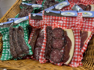 Villach, Avusturya - 01 Temmuz 2025: Hasır bir sepette değişik sosis ve salam içeren rengarenk damalı et paketleri
