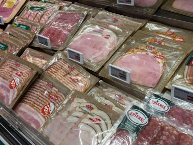 Villach, Avusturya - 01 Temmuz 2025: Süpermarket buzdolabında jambon, domuz pastırması ve salam içeren çeşitli meze ürünlerinin gıda sevenler için açık pakette sergilenmesi