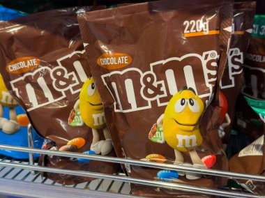 Villach, Avusturya - 01 Temmuz 2025: M & M 'nin çikolata şeker torbaları renkli ambalajlar ve neşeli karakterlerin altını çizerek bir mağaza rafına yerleştirilmiştir