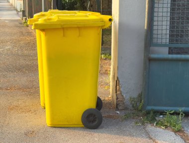 Sarı çöp bidonları güneş ışığında, çitle çevrili bölgede..