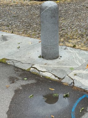 Şehir manzarası: kaldırım taşı caddesinde beton kazık ve su birikintisi.