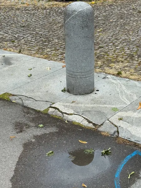 Şehir manzarası: kaldırım taşı caddesinde beton kazık ve su birikintisi.