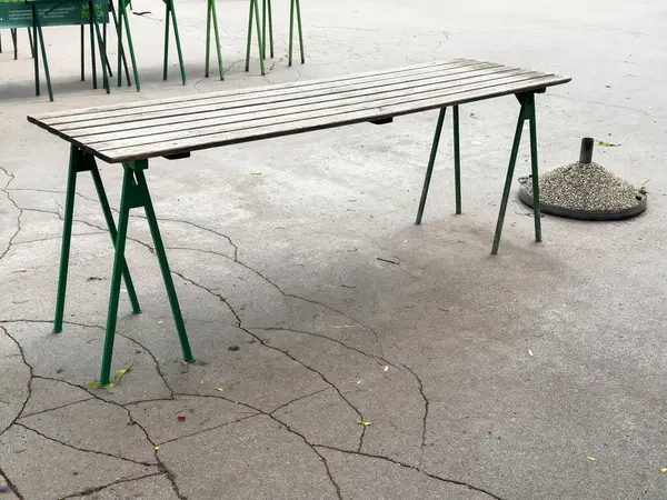 Boş ahşap masa, yeşil bacakları kırık kaldırımda, kül tablasının yanında..