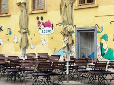 Ljubljana, Slovenya - Temmuz 06, 2025: Boş masaları ve sandalyeleri olan açık bir kafe, sarı duvarda canlı bir duvar resmi, akşam yemeği ve eğlence ortamını davet ediyor
