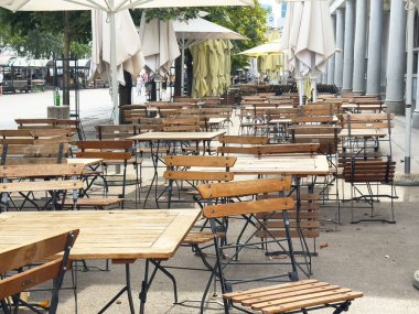Ljubljana, Slovenya - Temmuz 06, 2025: Boş ahşap masa ve sandalyeler şemsiyelerin altında sergileniyor ve misafirleri açık hava kafeteryasında yemek yemeye davet ediliyor