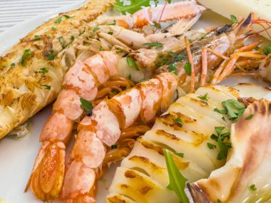 Karides, balık ve tabakta otlarla süslenmiş kalamar ile ızgara deniz ürünleri tabağı..