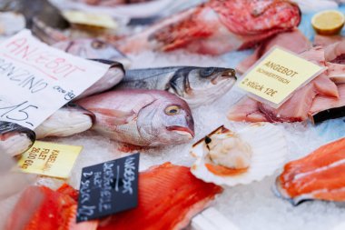 Villach, Avusturya - 11 Temmuz 2025: Buzdaki deniz ürünleri çeşitliliği fiyat etiketli balık ve kabuklu deniz ürünleri, canlı bir pazar ortamında tazelik ve çeşitliliği vurguluyor