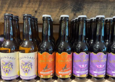 Villach, Avusturya - 10 Temmuz 2025: Ahşap raflarda farklı etiketlerle düzenlenmiş bira şişeleri, eşsiz tatlar ve canlı tasarımlar vurgulanıyor