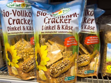 Villach, Avusturya - 10 Temmuz 2025: Süpermarket raflarında ayçiçeği tohumu ve peyniri içeren organik tahıl krakeri paketleri, sağlıklı abur cubur seçeneklerini teşvik