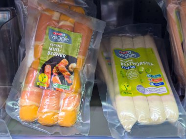 Villach, Avusturya - 10 Temmuz 2025: Süpermarket rafında açık ambalajlı vegan sosisleri, sağlıklı beslenmek için mini berner ve klasik sucuk seçenekleri sergileniyor