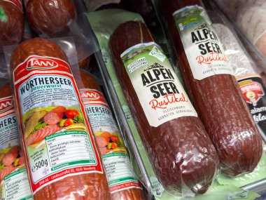 Villach, Avusturya - 10 Temmuz 2025: Alpen Seer ve Worthersee gibi paketlenmiş sosisler, Alman mutfak geleneklerini ön plana çıkaran bir market rafında düzgünce düzenlenmiştir.