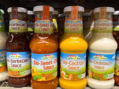 Villach, Avusturya - 10 Temmuz 2025: Mangal, acı biber, kokteyl ve sarımsak aromalı canlı ambalajlar içeren, market raflarında çeşitli organik soslar