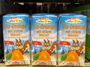 Villach, Avusturya - 10 Temmuz 2025: Spar Natur * pur Bio-Portakal suyu kutuları, canlı renklerle dolu bir market rafında sergilenen eğlenceli bir sincap tasarımı içerir.