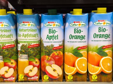 Villach, Avusturya - 10 Temmuz 2025: Süpermarkette elma ve portakal aromalı organik meyve suyu kutuları, taze malzemeler ve canlı ambalajlar