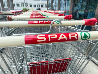 Villach, Avusturya - 10 Temmuz 2025: Parlak kırmızı sapları ve sağlam bir metalik tasarımı bulunan alışveriş arabaları bir SPAR mağazasının önünde düzgünce düzenleniyor