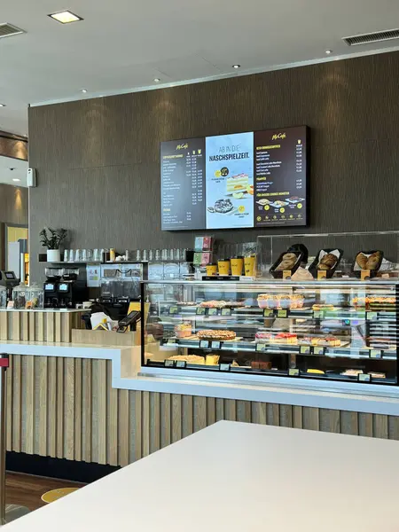 Villach, Avusturya - 12 Mayıs 2024: Çağdaş kafe sahnesi bir cam ekranın arkasında çeşitli hamur işleri ve içecekler sergiliyor, müşterileri eğlenmeye davet ediyor