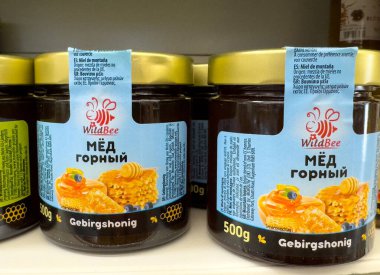 Villach, Avusturya - 15 Temmuz 2025: Yabanarısı bal kavanozları renkli etiketler ve bal peteklerinin yer aldığı bir mağaza rafına konur.