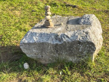 Güneşli bir çimenlikte büyük bir kaya üzerinde taş cairn.