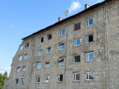 Yıpranmış duvarları ve temiz gökyüzünün altında uydu anteni olan harap bir bina..