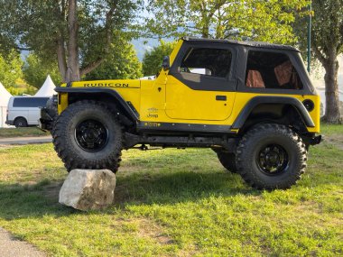 Villach, Avusturya - 20 Temmuz 2025: Sarı Jeep Rubicon çimenli bir arazide bir kayanın üzerinde konumlandırılmış, güçlü özelliklerini ve maceracı ruhunu vurguluyor
