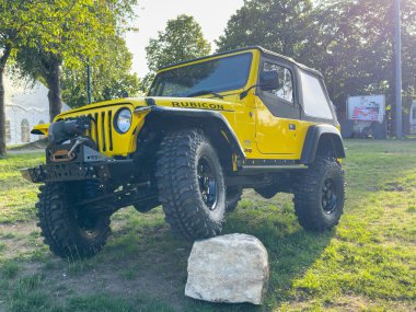 Villach, Avusturya - 20 Temmuz 2025: Sarı Jeep Rubicon bir kayanın yanındaki çimlerin üzerinde duruyor ve manzaralı bir ortamda sağlam özelliklerini ve off-road hazırlığını vurguluyor