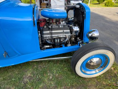 Villach, Avusturya - 20 Temmuz 2025: Mavi otomobil parlak bir motor ve krom aksanlı, çimlerin üzerine park edilmiş, klasik otomotiv tasarımı ve işçiliği sergilenmektedir